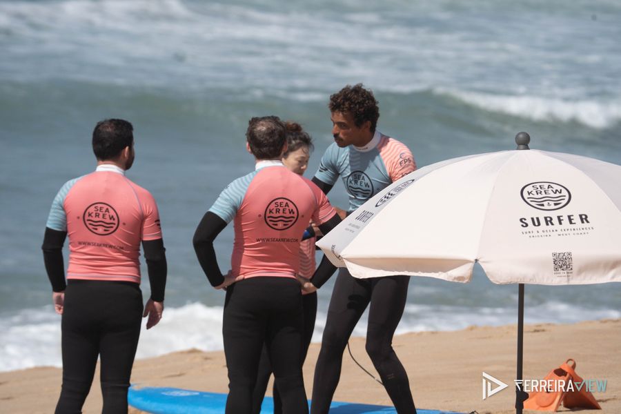 Aula de surf da Sea Krew na praia: o instrutor explica a técnica ao grupo