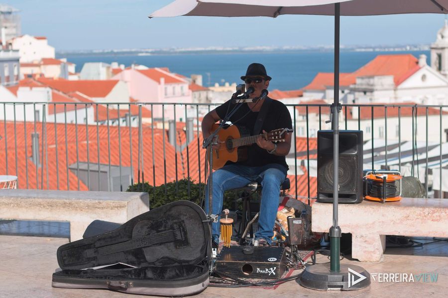 Músico de rua num miradouro de Lisboa, com o Tejo ao fundo