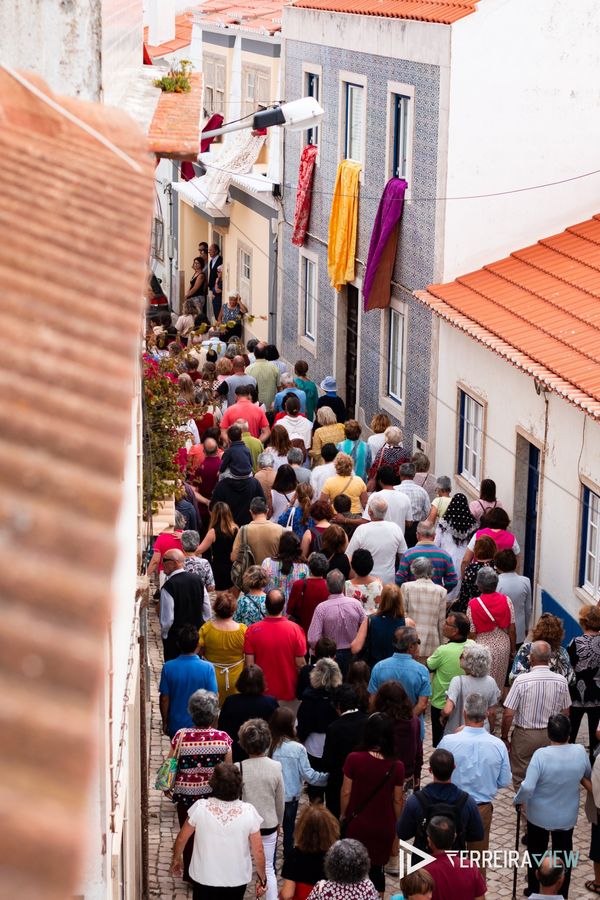 Procissão numa rua estreita, com colchas penduradas nas janelas